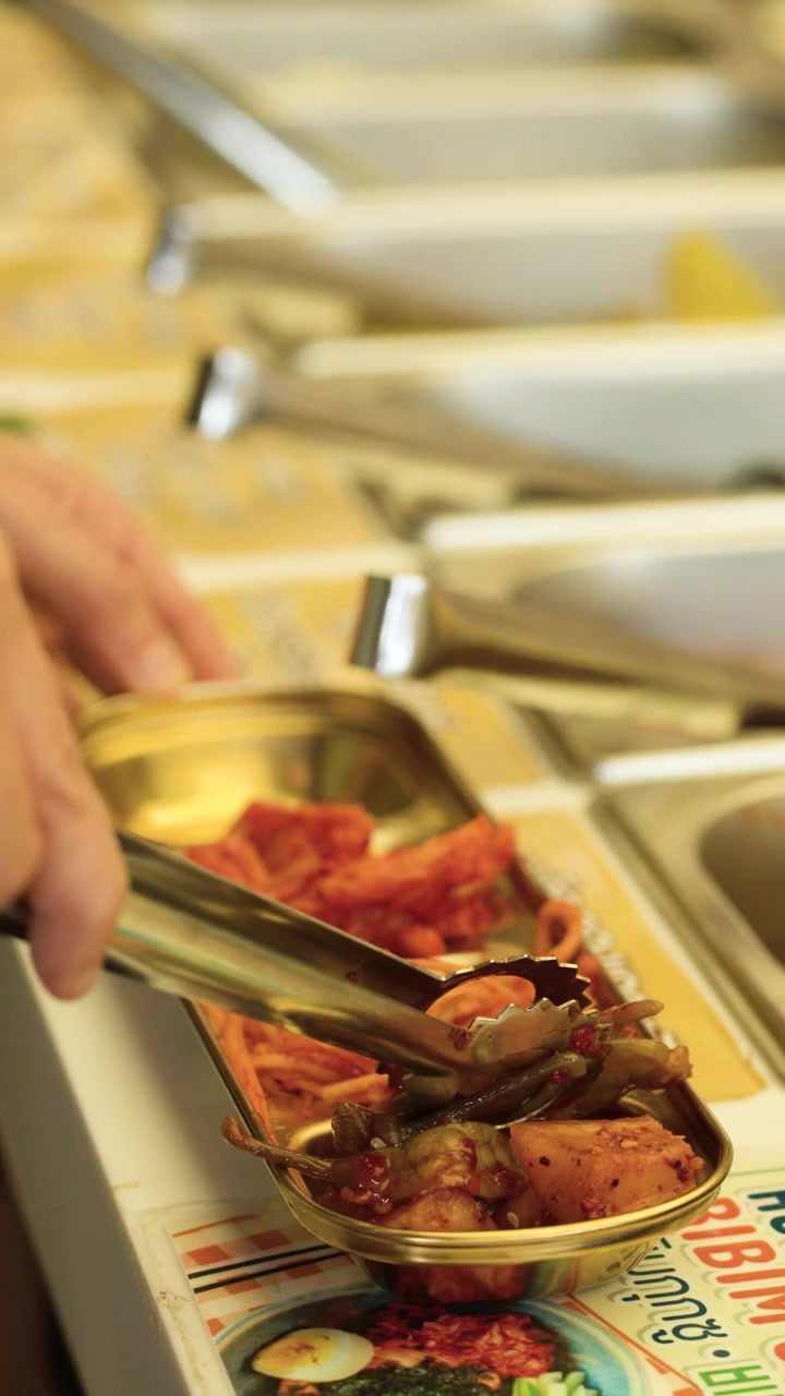 Persona che usa le pinze per servire contorni coreani a un buffet