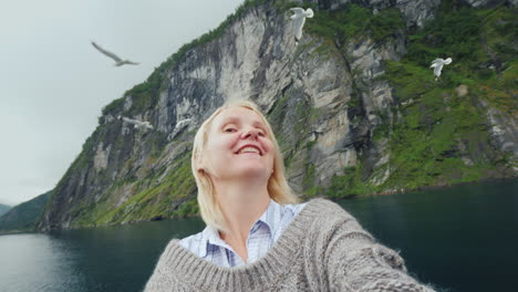 a woman takes pictures of herself against the backdrop of the norwegian fjord travelling on a cruise