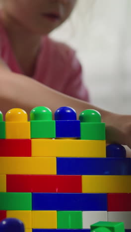 cute girl takes colorful plastic blocks to build structure on blurred background. brother moves built fortress wall with heavy machine toy closeup