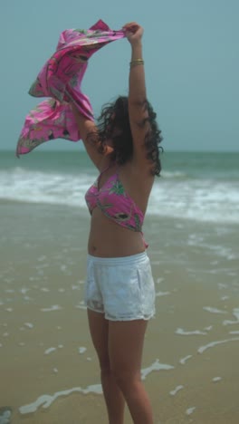 woman enjoying beach breeze, holding bright pink scarf with tropical pattern