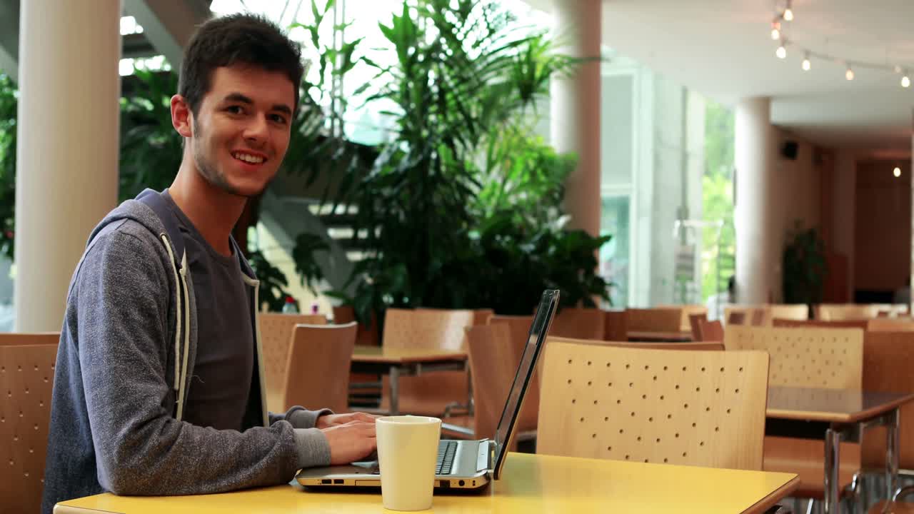 Estudante sorrindo, sentado e usando seu laptop