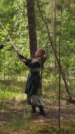 young nobleman trains sword strikes with teacher in green wood slow motion. teenage boy and man role playing. middle age lifestyle reconstruction