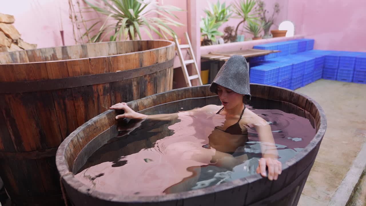 Giovane donna che si immerge ed esce da una tinozza spa in legno