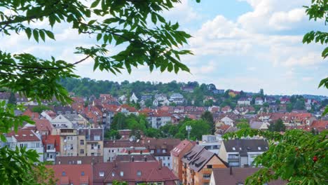 pan-on-city-of-stuttgart,-green-trees-in-foreground-and-cumulus-clouds-in-the-sky