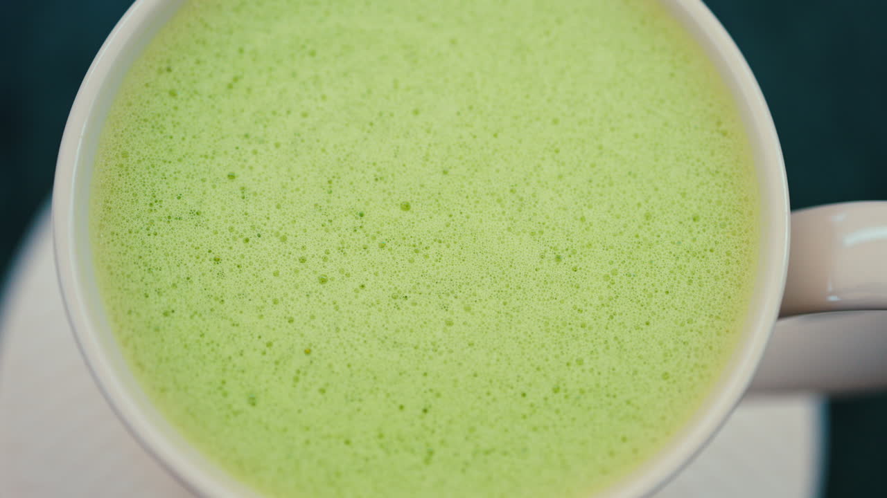 Close up of a smooth matcha latte with vibrant green foam in a white cup