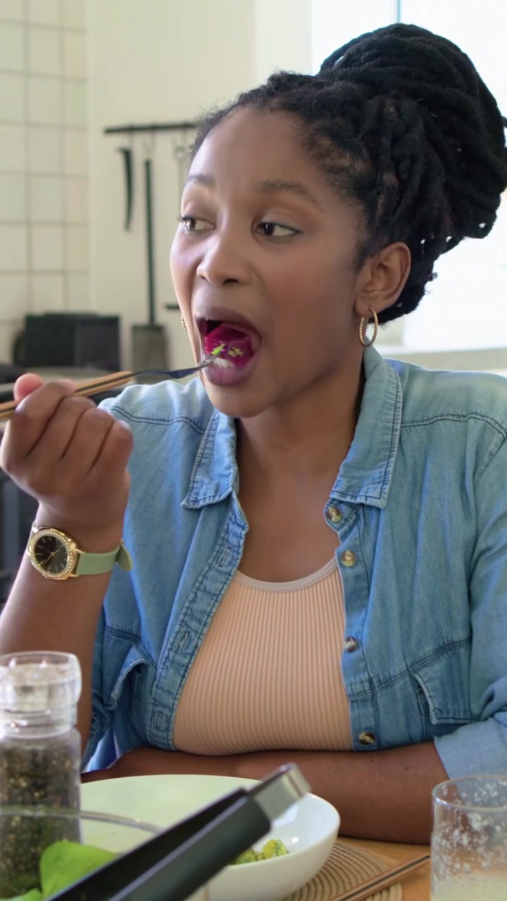 Vertical video: Stirring woman mixing salad then eating at dining table, responding to prompt