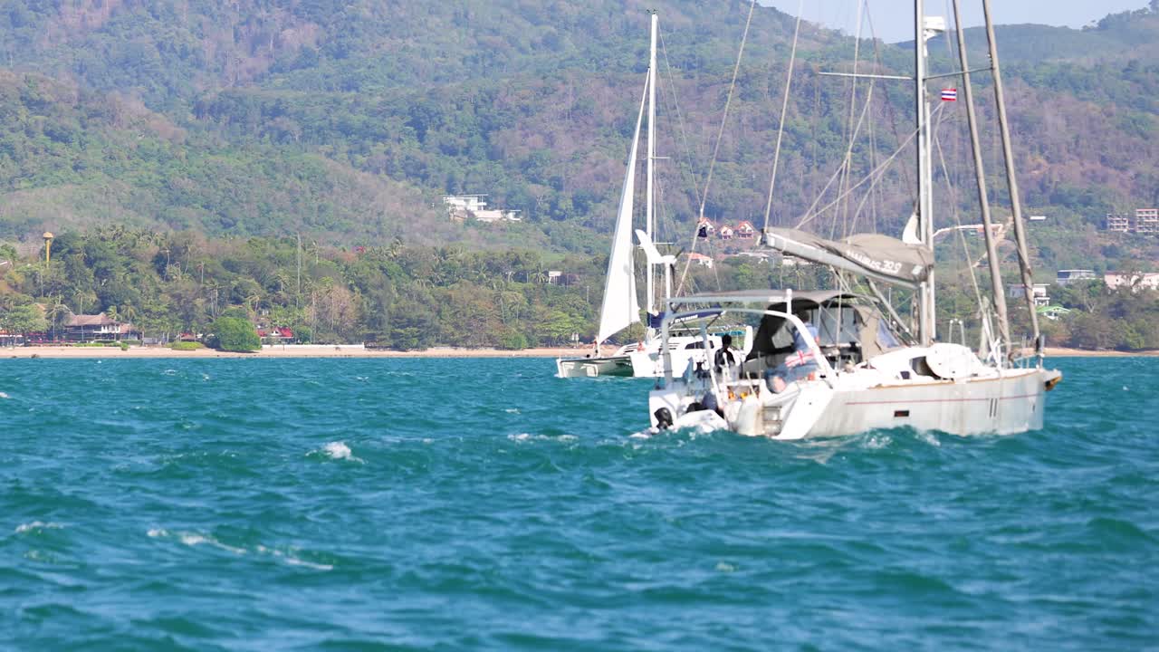 태국 푸켓 근처의 활기찬 파란 바다를 항해하는 요트, 은 하늘 아래 잔잔한 언덕이 배경으로