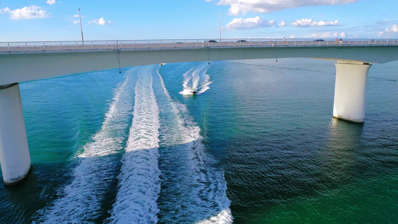 Power boats traveling under a bridge on a sunny blue day