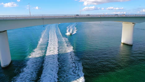 power boats traveling under a bridge on a sunny blue day