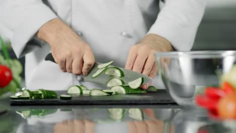 Male-chef-cutting-fresh-vegetable.-Closeup-chef-hands-slicing-cucumber.