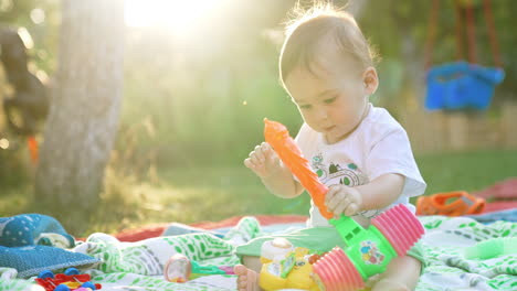 charming little boy playing with his toys on the plaid in the garden. beautiful caucasian child in the rays of summer sun. blurred backdrop.