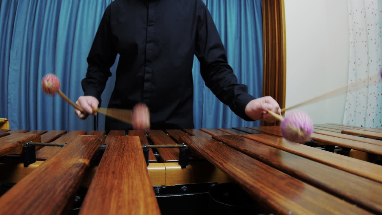 남성 타악기 연주자가 검은색 셔츠를 입고 마림바에서 아르페지오를 연주하고 있습니다.
