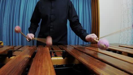 a male percussionist is playing arpeggios on marimba wearing a black shirt