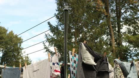 Detail-of-laundry-attached-with-nippers-hanging-to-dry-in-a-garden-on-a-foldable-rotating-drying-rack-with-lines-and-cords-with-trees-and-blue-sky-in-the-background