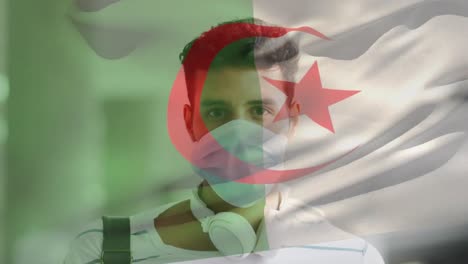 animation of flag of algeria waving over man wearing face mask during covid 19 pandemic