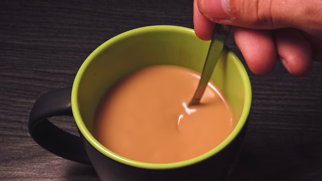 Primo piano al rallentatore di un uomo che mescola caffè nero con latte su un tavolo di legno in cucina