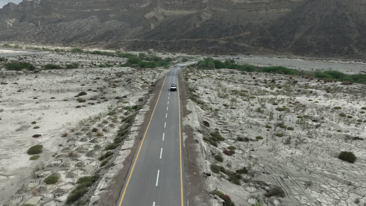 공중 드론은 뒤로 움직이고 구름이 많은 날 발로치스탄의 배경에 산맥과 함께 힌골 국립 공원의 고속도로를 따라 움직이는 차 위에서  ⁇ 습니다.