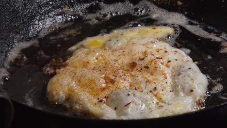 closeup: crispy fried egg removed from hot buttery pan with spatula