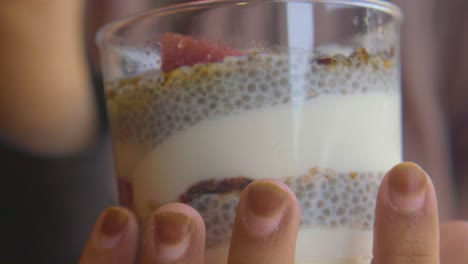 close up shot of a hand holding a glass of chia pudding with berries and granola