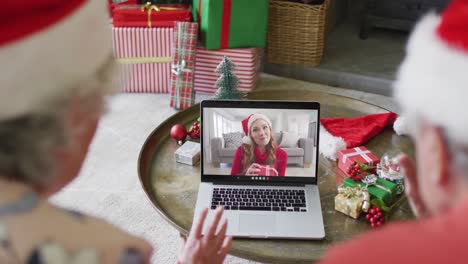 Senior-caucasian-couple-with-santa-hats-using-laptop-for-christmas-video-call-with-woman-on-screen