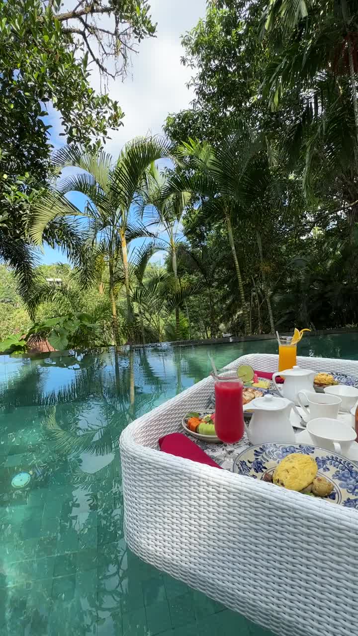 Experience a luxurious floating breakfast in a tropical infinity pool surrounded by lush jungle in Ubud, Bali. This vertical video captures serene, colorful ambiance perfect for social media