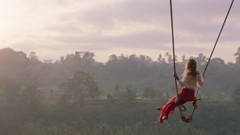 travel woman swinging over tropical rainforest at sunrise female tourist sitting on swing with scenic view enjoying freedom on vacation having fun holiday lifestyle slow motion