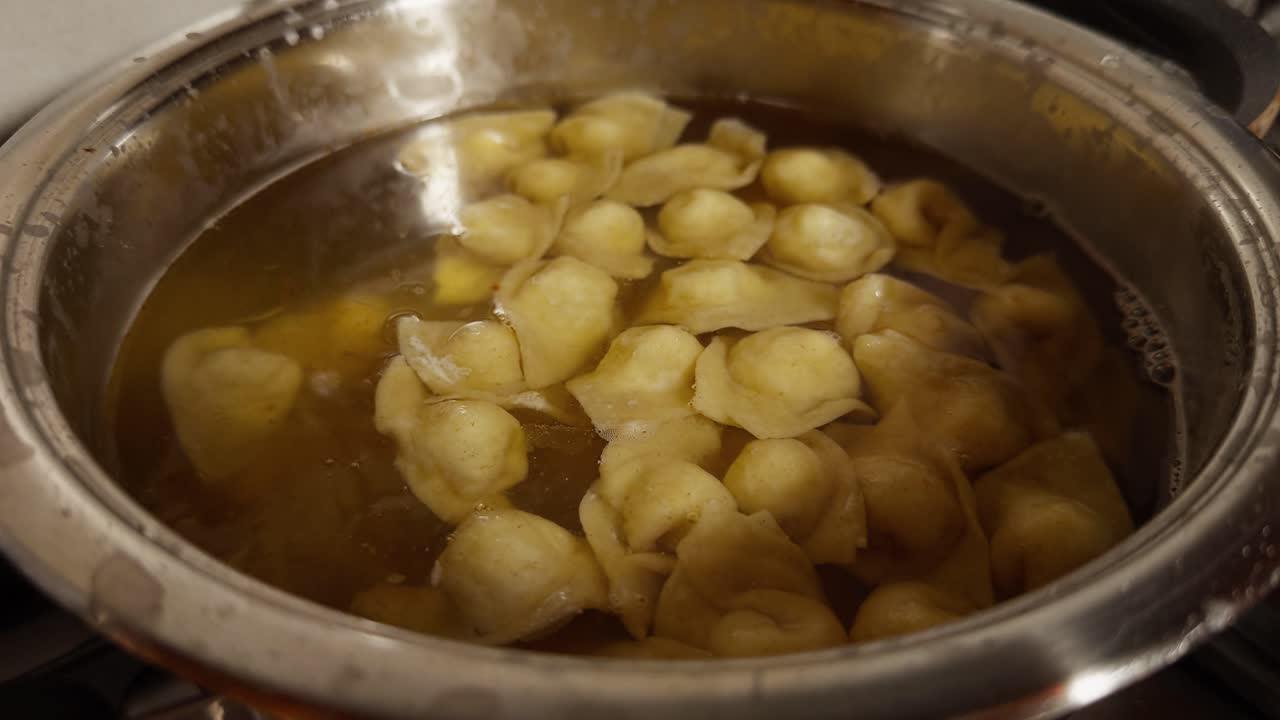 I cappelletti cuociono lentamente in un brodo leggero, che galleggiano all'interno di una pentola di metallo sul fornello di una cucina tradizionale