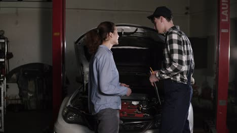 Cute-car-or-automotive-technician-wearing-work-robe-and-a-cap-is-meeting-with-his-female-clients-and-hears-out-complaints-about