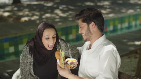 Romantic-muslim-couple-sitting-on-bench,-feeding-each-other.