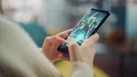 close up on a person hands playing an arcade video game on a vertically held smartphone at home living room. feminine hands tapping the mobile phone screen with a colorful game over the internet.