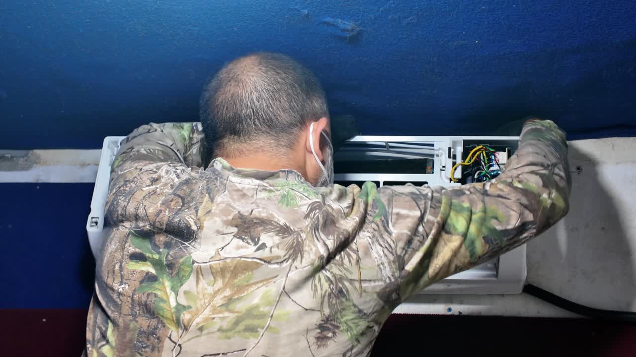 Man opening air conditioner unit with a power tool to perform internal cleaning and maintenance on the system