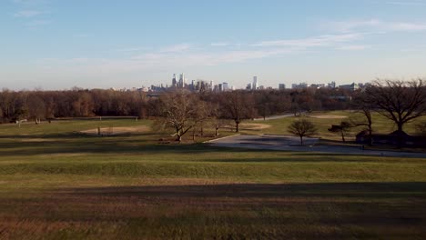 a beautiful aerial drone shot, drone flying low over a park towards the philadelphia skyscraper skyline, pennsylvania