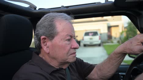 close-up of older age man turns and pulls onto the road in his convertible suv