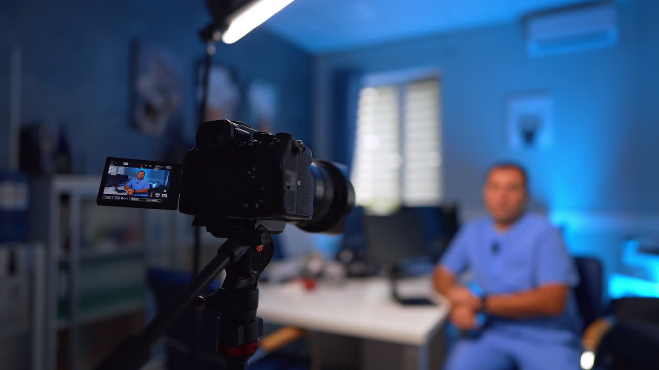 Digital camera with display recording a video of man. Close up. Medic wearing blue uniform creates vlog for colleagues and patients. Selective focus
