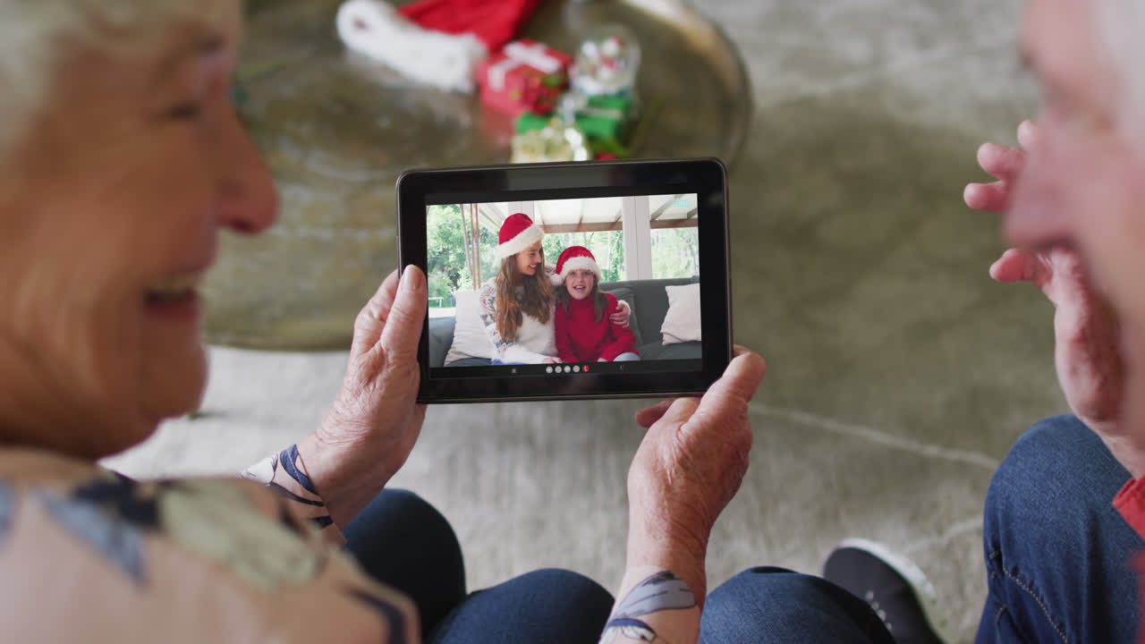 Coppia anziana caucasica che usa un tablet per una videochiamata di Natale con una famiglia felice sullo schermo