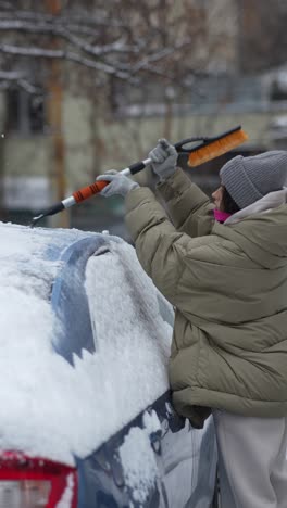 woman removing snow from car in winter