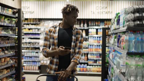 Handsome-man-with-smartphone,-pushes-shopping-cart,-walks-at-the-store