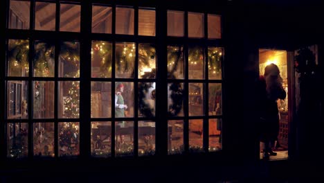 christmas time. santa with bag full of presents comes out of his residence. santa in red costume is going to children at christmas night. view from outdoors.