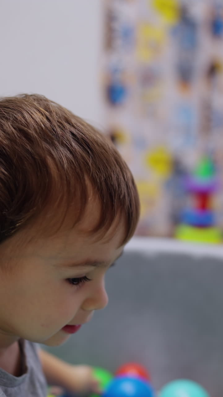 Bambino sdraiato nella piscina asciutta che si siede. Bambino adorabile che lancia la palla in avanti. Sfondo sfocato. Video verticale