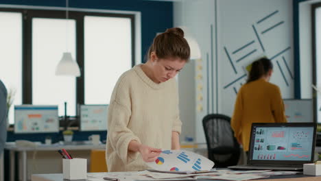 busy woman in startup office holding clipboard looking at papers with sales charts