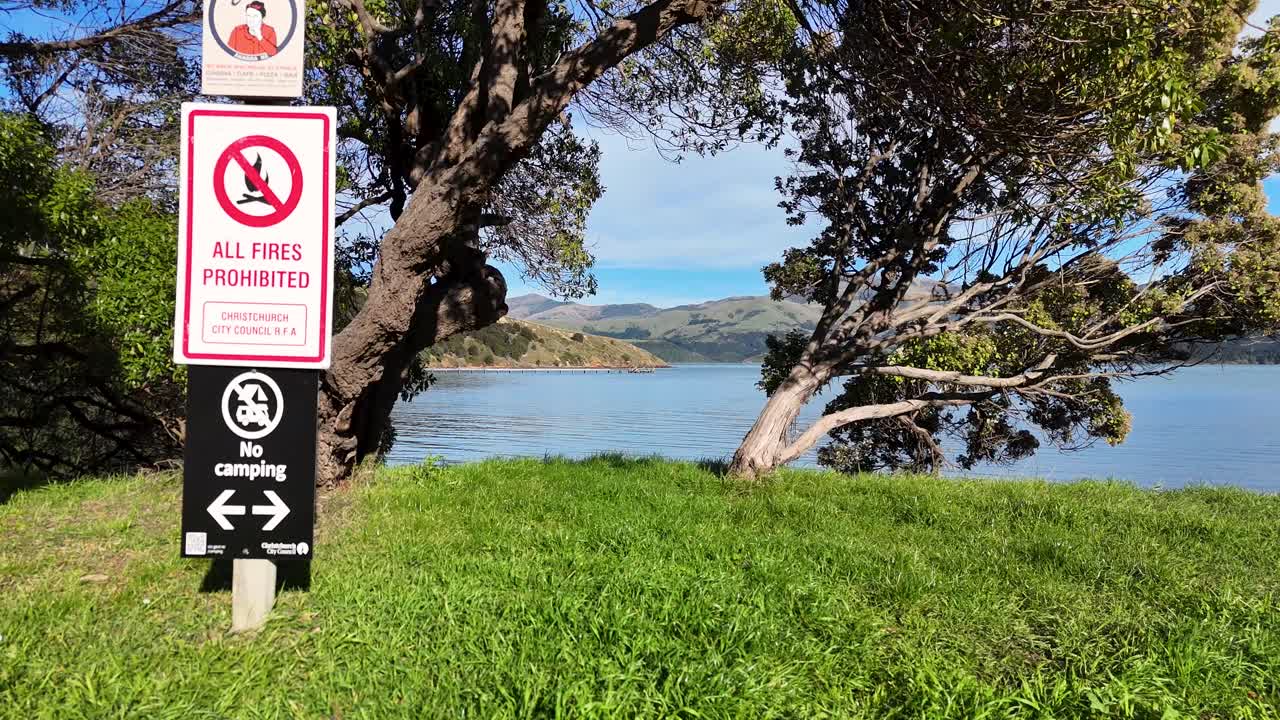 A serene aerial view of Akaroa's lake, surrounded by lush greenery and mountains under clear blue skies