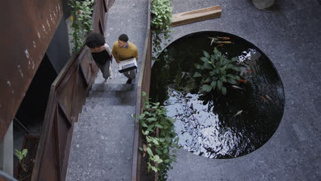 Diverse-male-and-female-colleague-walking-up-stairs-using-laptop,-talking,-copy-space,-slow-motion