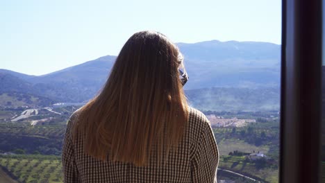 caucasian girl with straight hair and a checkered coat with her back to the camera on a sunny background of mountains and fields