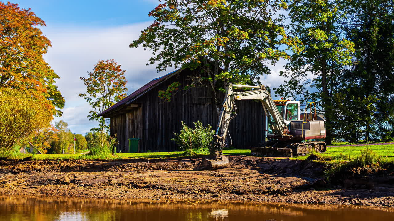 Truck unloads dirt at a rural construction site with autumn trees in a timelapse view