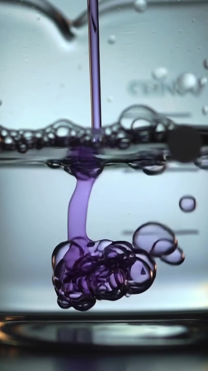 Vidéo verticale : Un tube injecte un colorant violet formant un panache dans un bécher gradué de laboratoire, montrant des bulles.