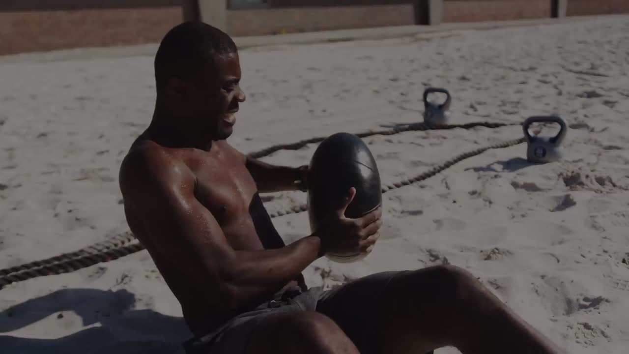 Colorful spots of light against african american fit man working out with medicine ball at the beach