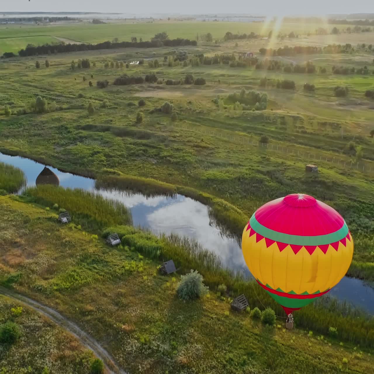 Aerostat on nature background. Colorful hot air balloon flying over the field near the small river. Outdoor activity. Top view. Camera moves down.