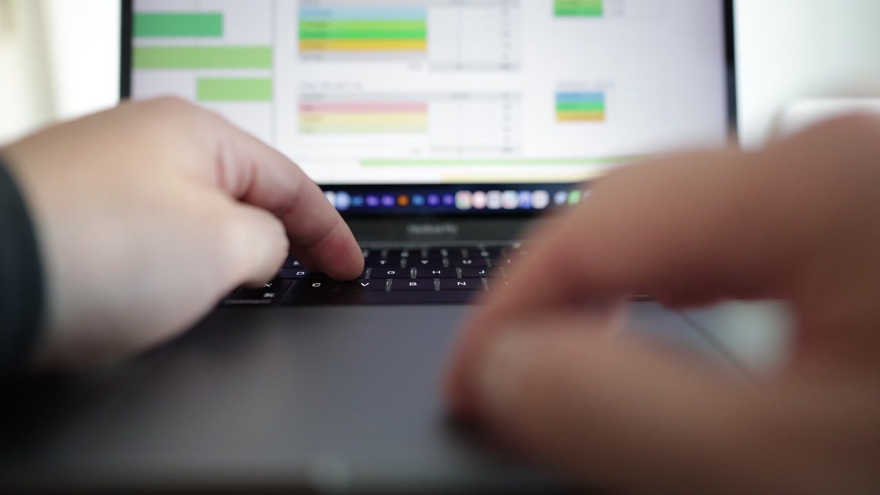Vista em close-up de um laptop exibindo um painel de análise de negócios com estatísticas, gráficos de pizza e dados de desempenho. Mãos digitam no teclado enquanto usam o mouse para clicar e rolar.