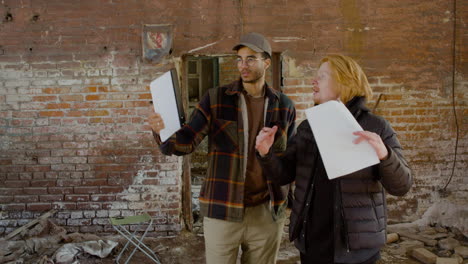 two production coworkers talking and reading a document about the movie in a ruined building