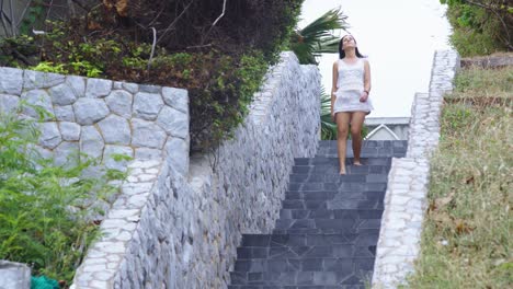 young brunette woman wearing white clothes walking down the stairs in tropical area on windy day